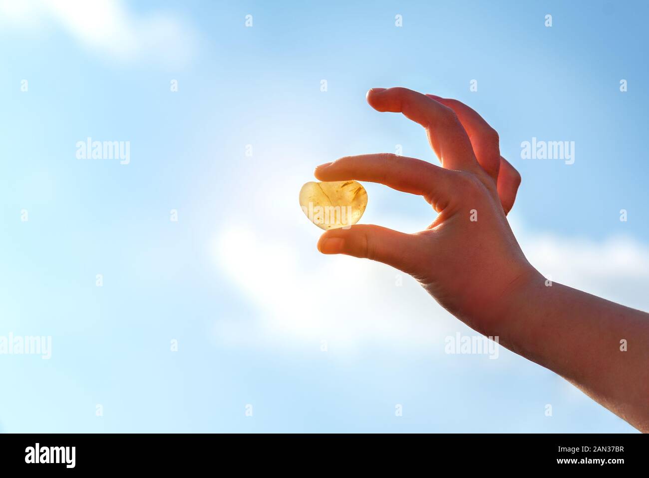 Cuore di pietra a forma di detenuti in mani, cielo blu in background. Rockhounding visualizza una pietra che consente alla luce di viaggiare attraverso di esso. Foto Stock