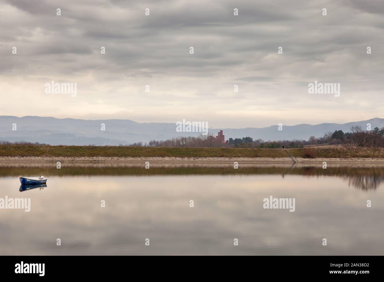 Vista unica sul lago Kragujevac, calmo e riflettente, con vecchia barca blu durante una giornata torbida e brulica, nel museo commemorativo 21st ottobre a Sumarice Foto Stock