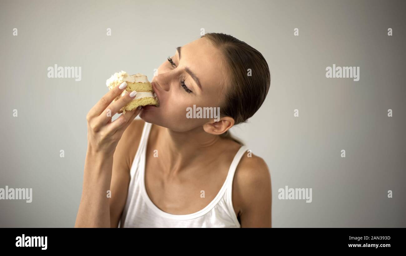 Slim ragazza di mangiare la torta con trepidazione, dieta e fame, mancanza di autodisciplina Foto Stock
