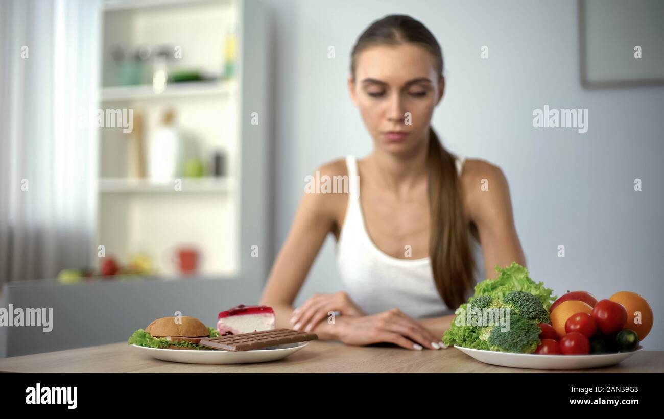 Slim ragazza scegliendo tra il cibo spazzatura e ortaggi sani, strappi, dieta Foto Stock