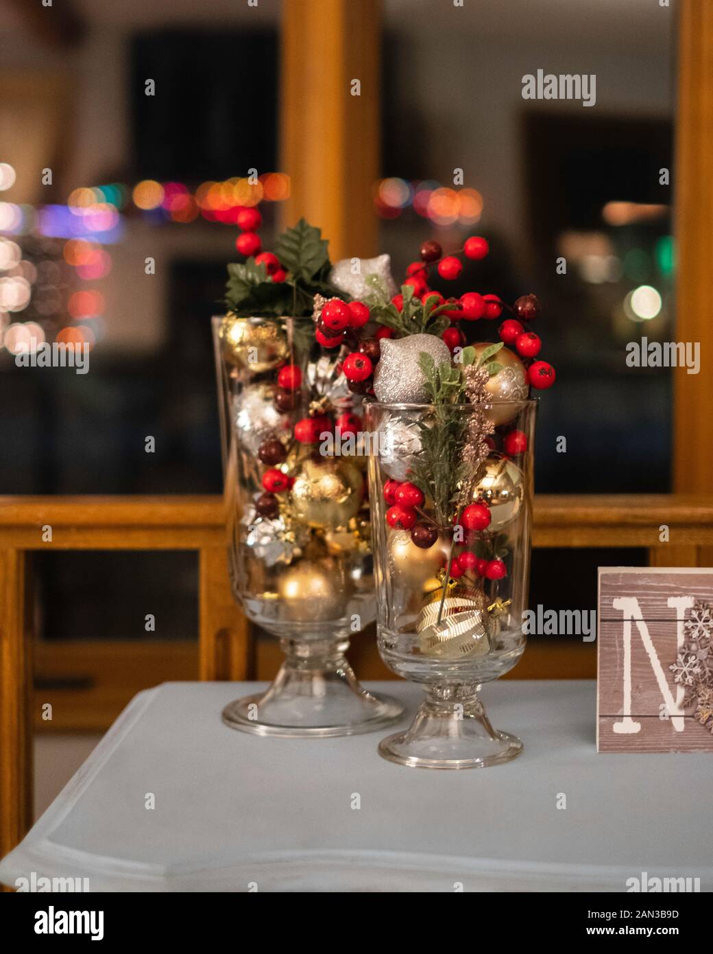 Due candelieri di vetro riproposto pieni di palle di Natale d'oro e d'argento e bacche di oly, decorazioni natalizie. Foto Stock