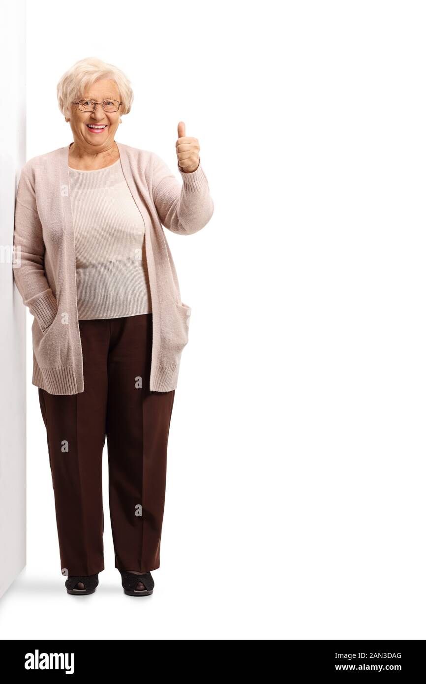 Ritratto a tutta lunghezza di una signora anziana appoggiata alla parete e scritta gesturante su un pollice isolato su sfondo bianco Foto Stock