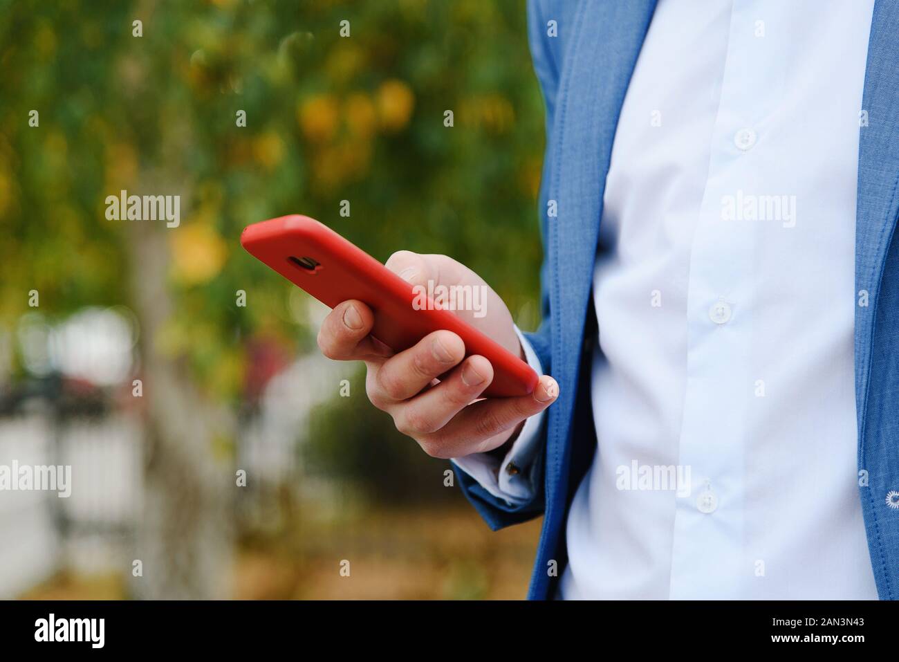 L'uomo utilizza lo smartphone all'aperto. Manager tenere in mano il telefono in caso di colore rosso. Mano maschio con telefono close-up. Foto Stock