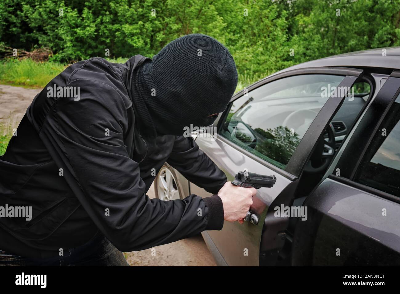 Il furto di auto in maschera nera con una pistola apre la porta in auto Foto Stock