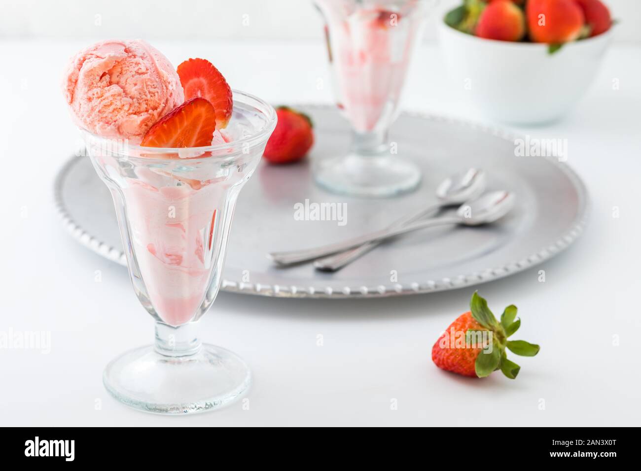 Un vetro piatto da dessert riempito con gelato alla fragola gelato con un altro su un vassoio di metallo in dietro. Foto Stock
