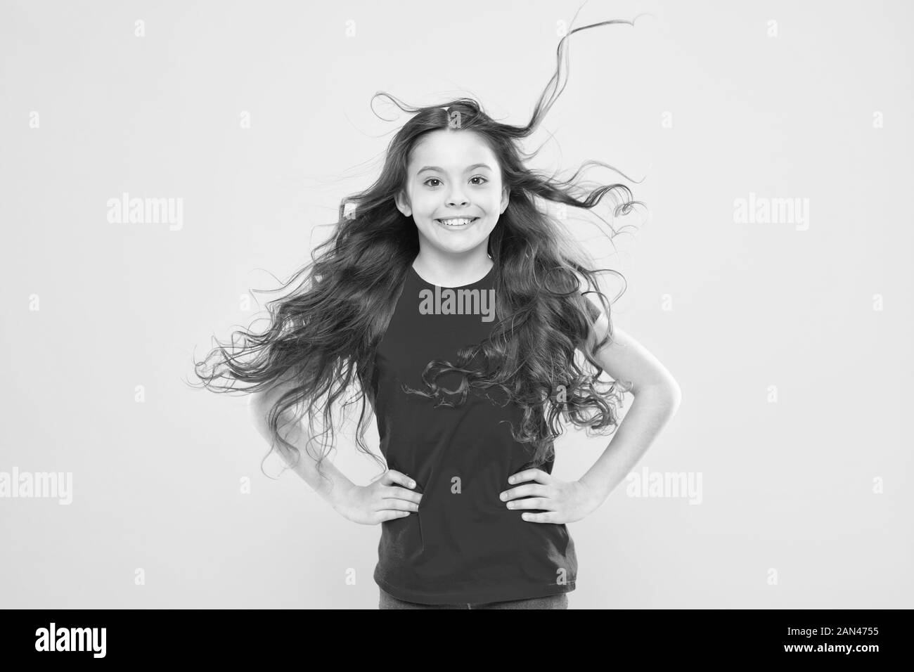 Interessato a i miei capelli e la mia parrucchiera. Felice piccolo bambino ragazza sorridente con fluente lungo brunette capelli su sfondo giallo. Kids parrucchiere. Salone di Parrucchiere. Foto Stock