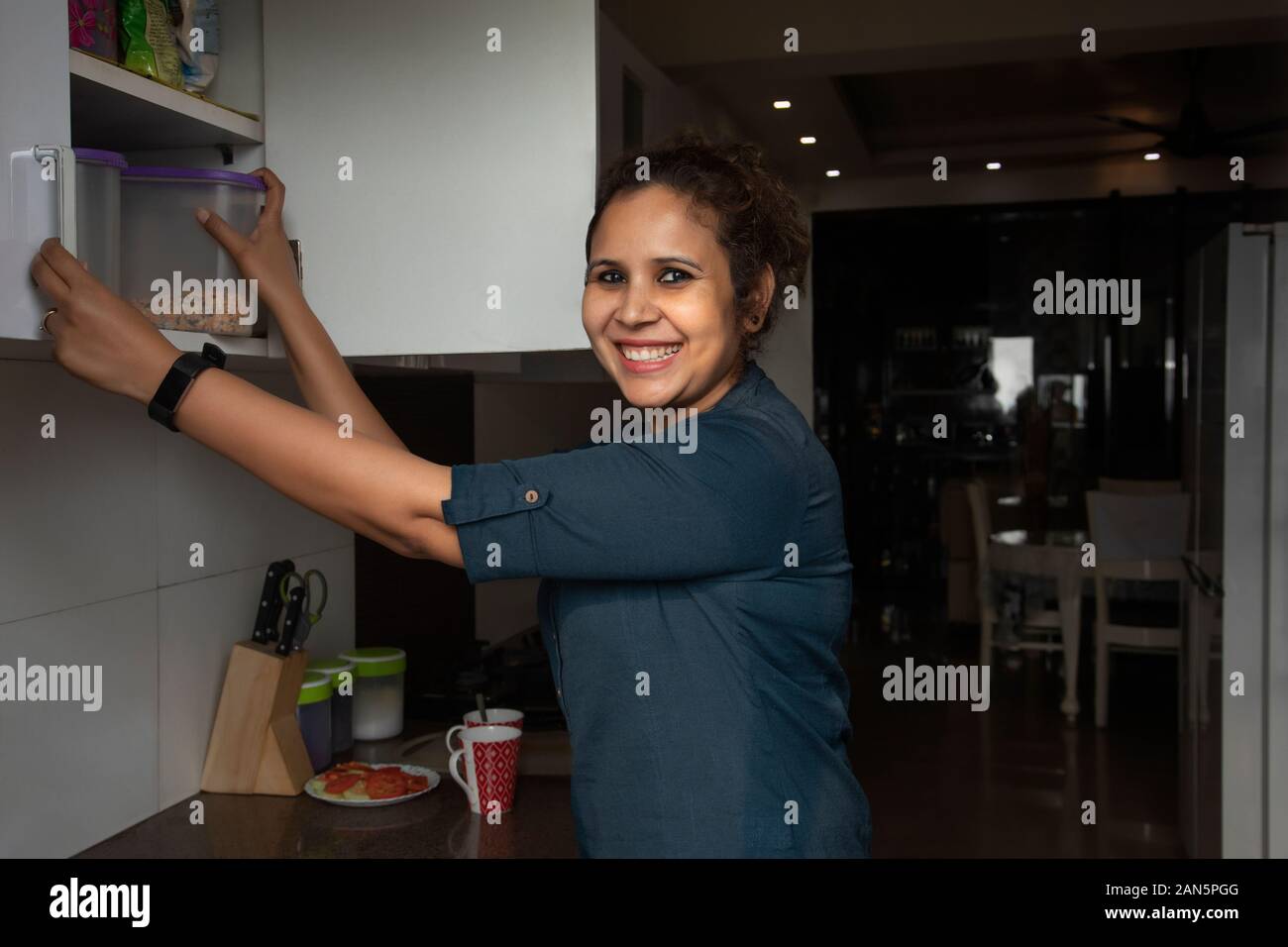 La donna tirando fuori uno spuntino scatola dalla credenza in cucina Foto Stock