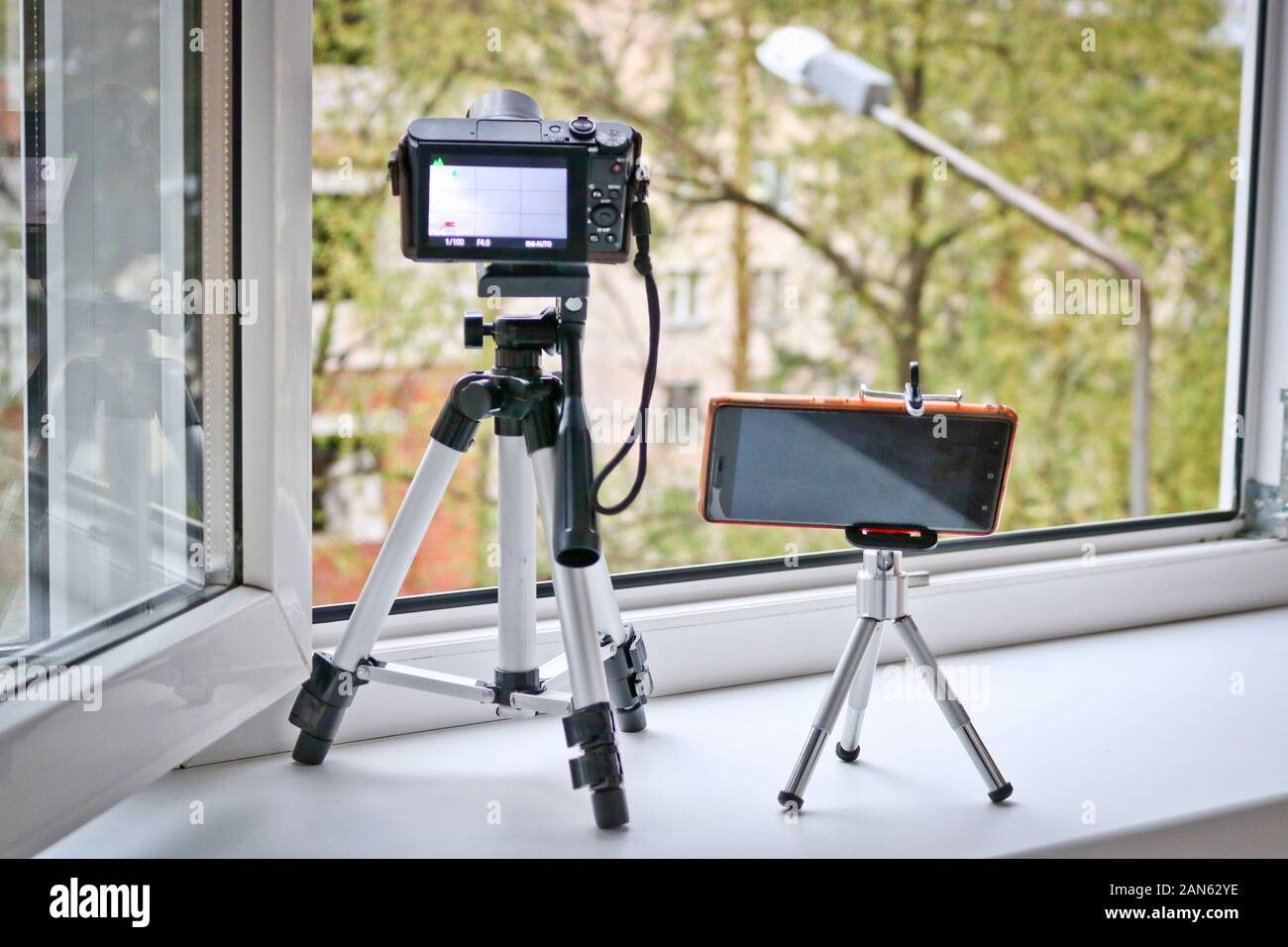 Fotocamera e smartphone su cavalletti di fronte a una finestra aperta. Time Lapse photography - smartphone vs fotocamera. Foto Stock