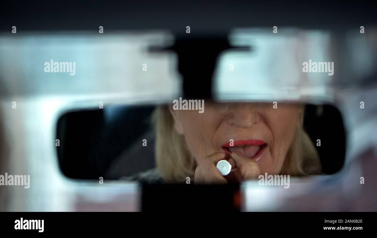 Elegante lady senior di preparare per la data, il rossetto, cercando in specchio auto Foto Stock