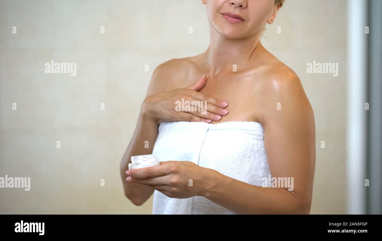 Donna di mezza età massaggianti e applicando l'idratazione lozione per il corpo nella stanza da bagno Foto Stock