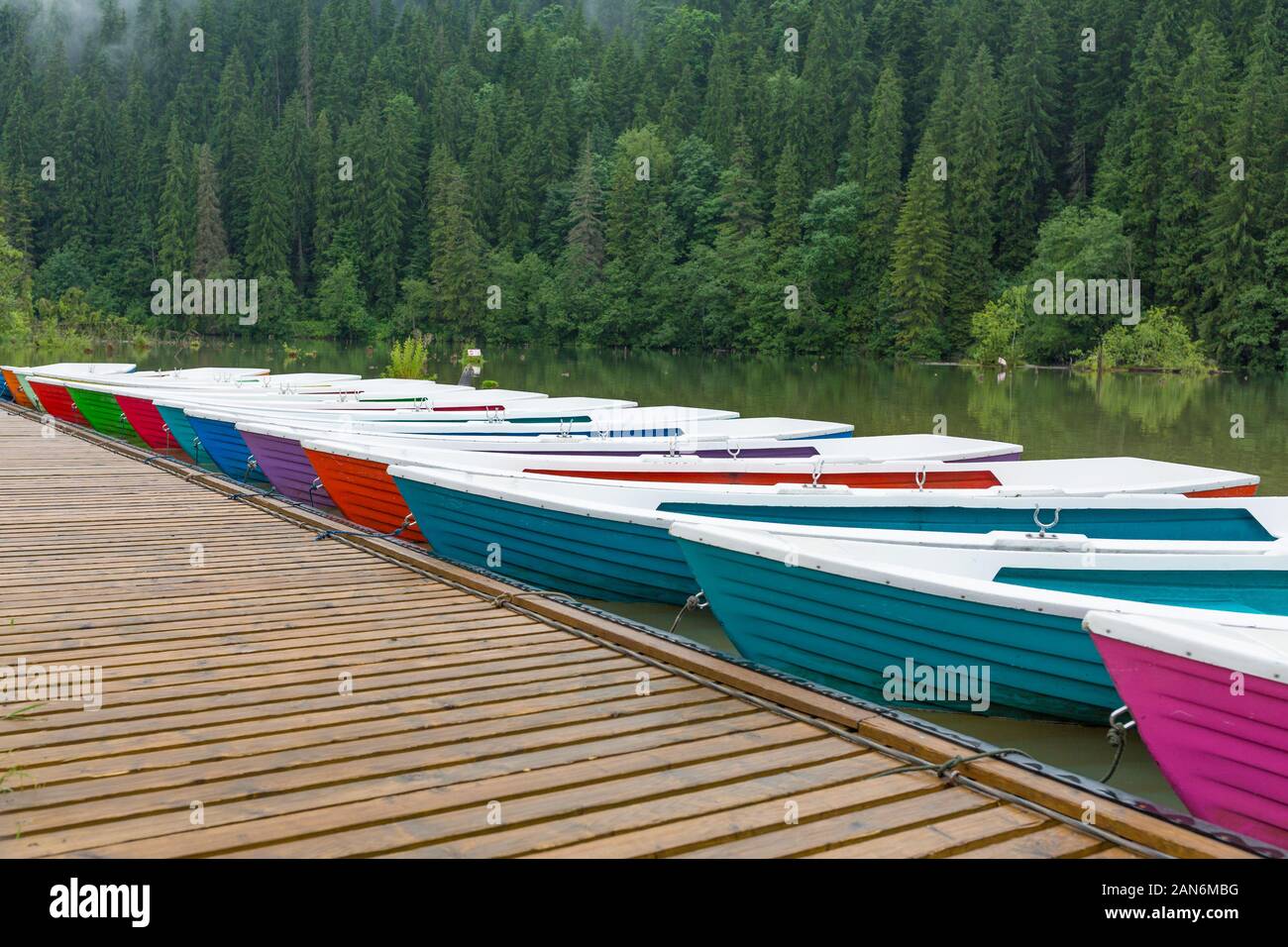 Barche colorate / barche a remi, allineate al lago rosso in transilvania. Carpazi boschi sullo sfondo. Scenario tranquillo. Destinazione di viaggio. Foto Stock
