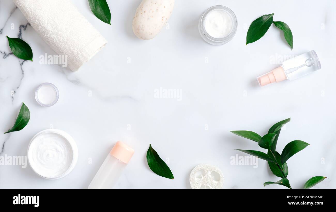 Prodotti di Cosmetica Naturale e foglie verdi su sfondo marmo. Cornice fatta di asciugamani, sapone artigianale, olio essenziale, spugna Luffa, Crema mani. Lay piatto Foto Stock