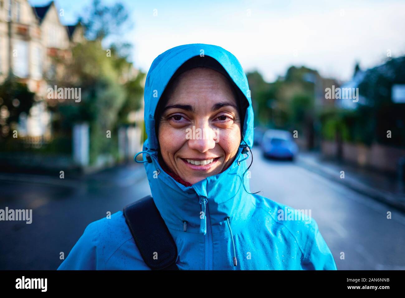 Bianco sorridente donna che indossa un blu giacca impermeabile in strada Foto Stock