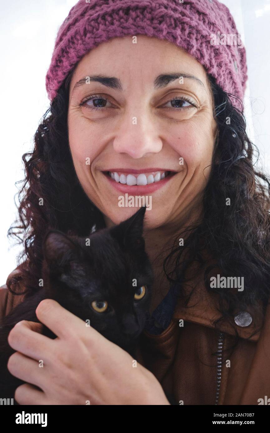 Lei guarda la fotocamera per un ritratto con il suo gatto nero Foto Stock