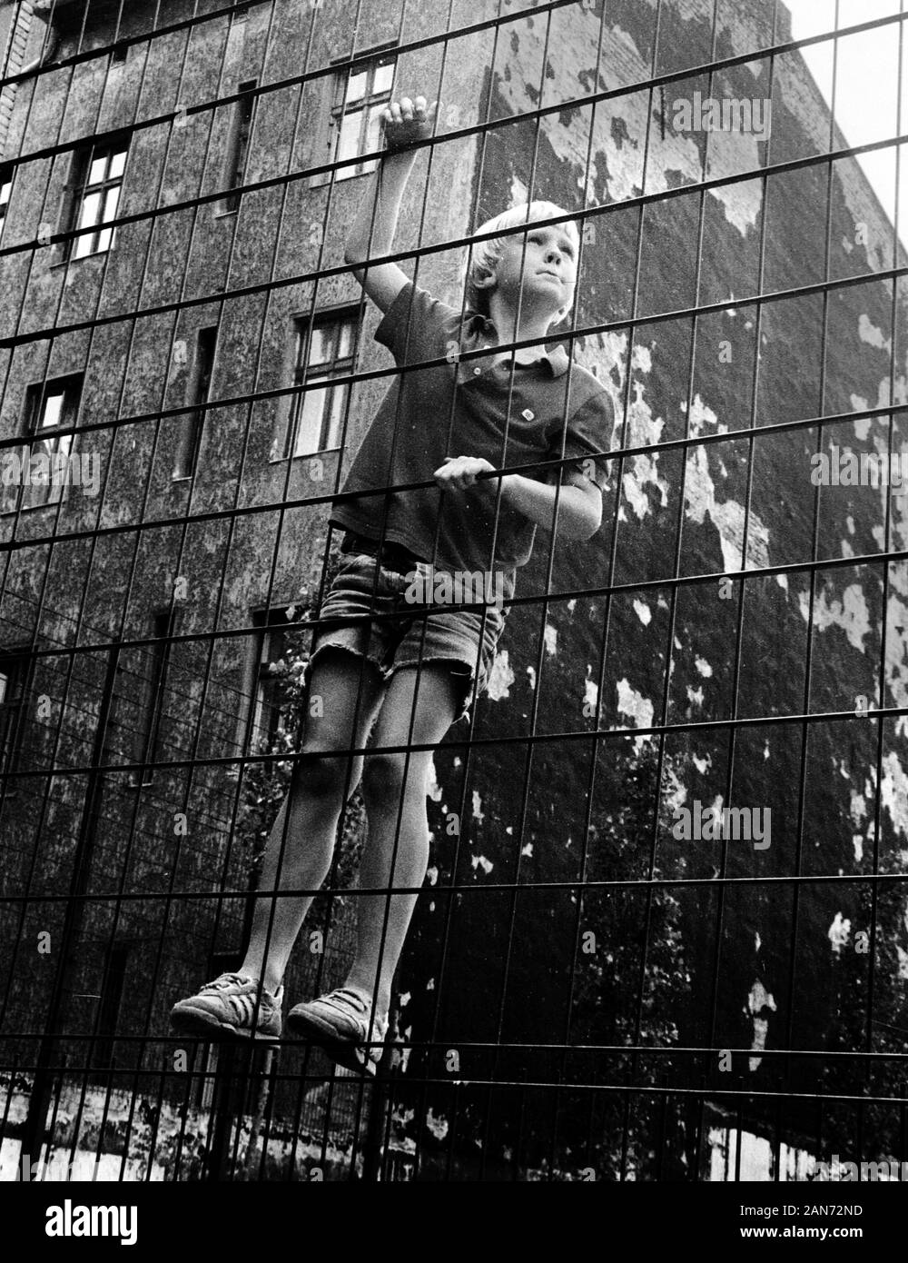 01 gennaio 1988, Berlin: un ragazzo si arrampica una recinzione in un cortile. Luogo e data di registrazione non esattamente noto. Foto: Paul Glaser/dpa-Zentralbild/ZB Foto Stock