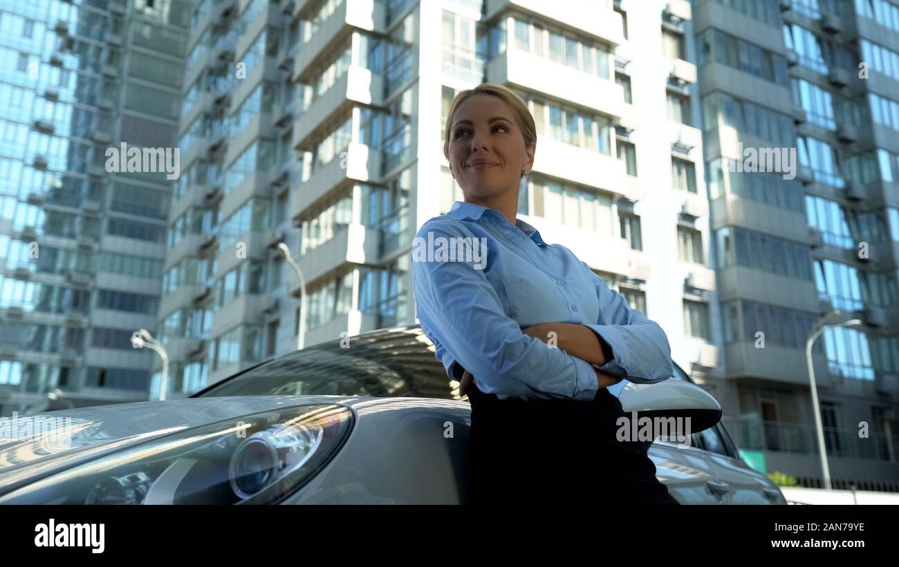 Fiducioso lady in business suit in piedi poggiando sulla nuova vettura, il successo e il benessere Foto Stock