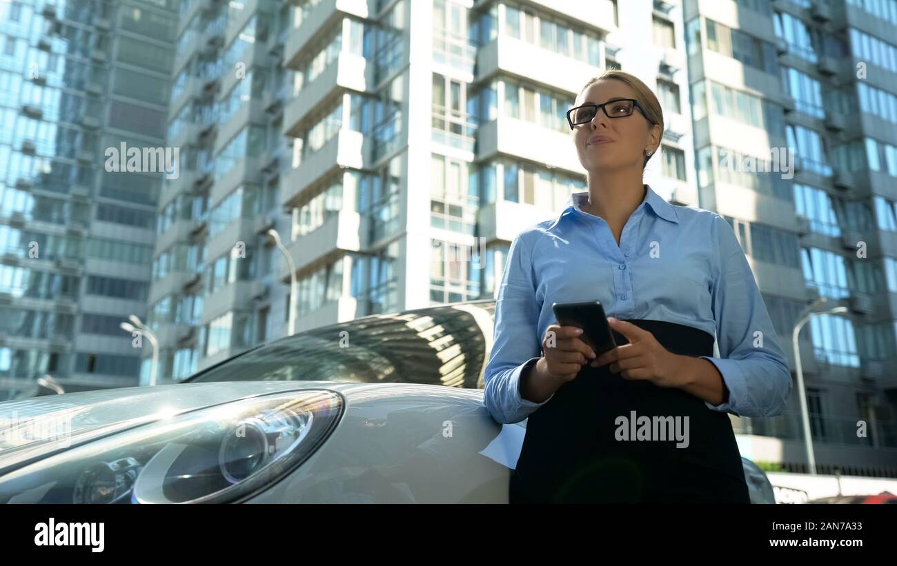 Signora occupato con lo smartphone pensando ai piani in piedi vicino alla sua auto, business Foto Stock