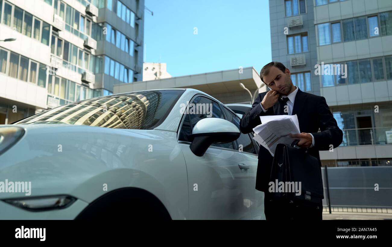 Uomo di occupato la lettura di carte nella sua mano parlando al telefono, problematiche aziendali della società Foto Stock