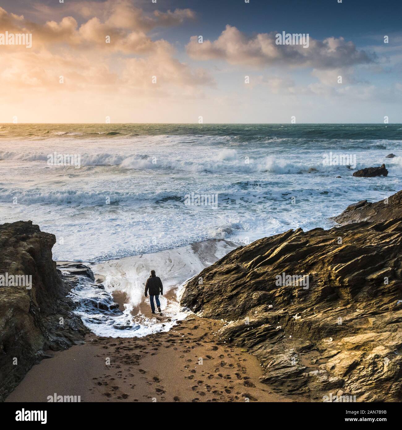 Un uomo che cammina verso il basso per il litorale e guardando le onde in arrivo in un mare increspato a poco Fistral a Newquay in Cornovaglia. Foto Stock