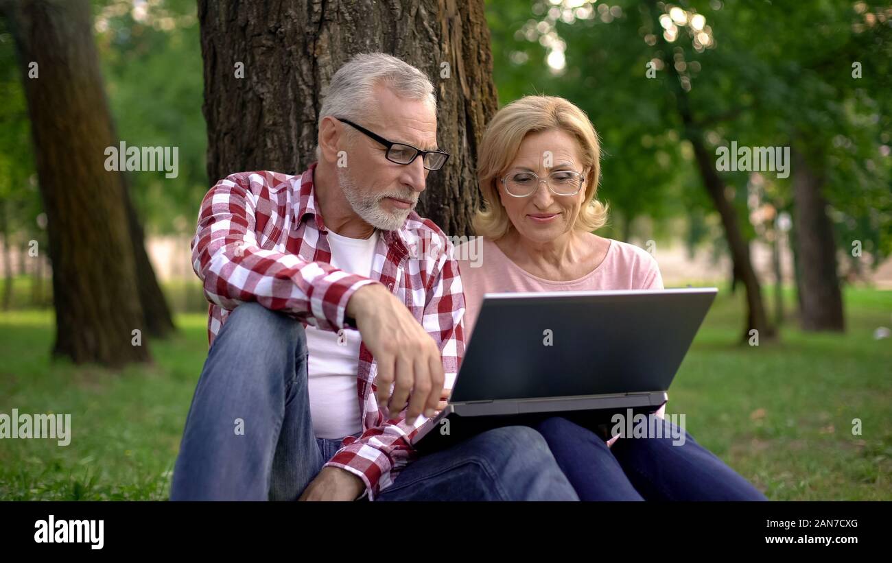 Nonni in appoggio nel parco e guardare interessante video sul pc portatile per app Foto Stock