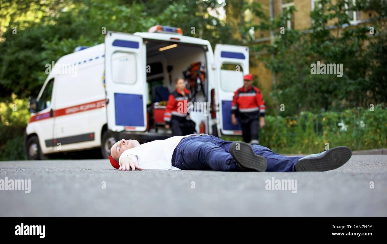 Giovane uomo disteso sulla strada, paramedici in esecuzione per la vittima di un incidente automobilistico, primo soccorso Foto Stock