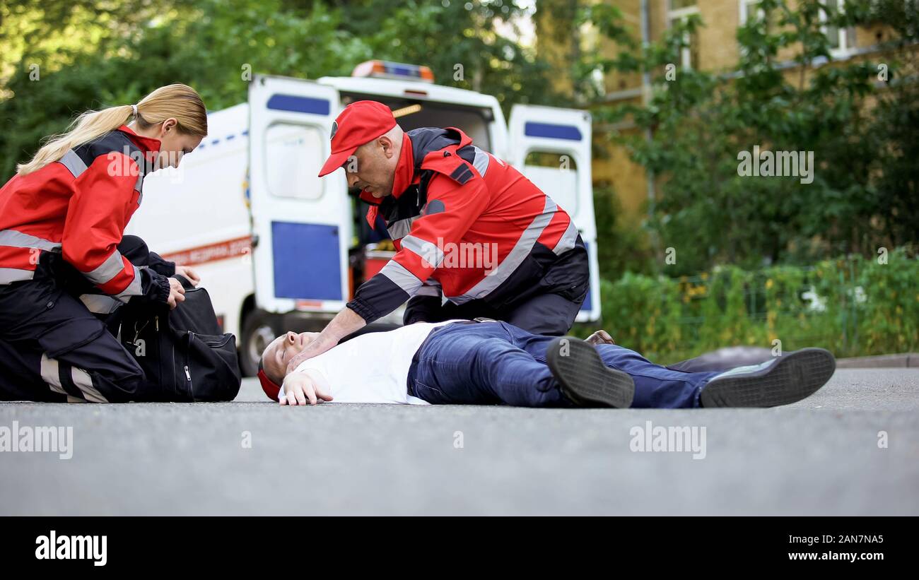 I medici che forniscono assistenza urgente all uomo incosciente, attacco di cuore o di incidente di automobile Foto Stock
