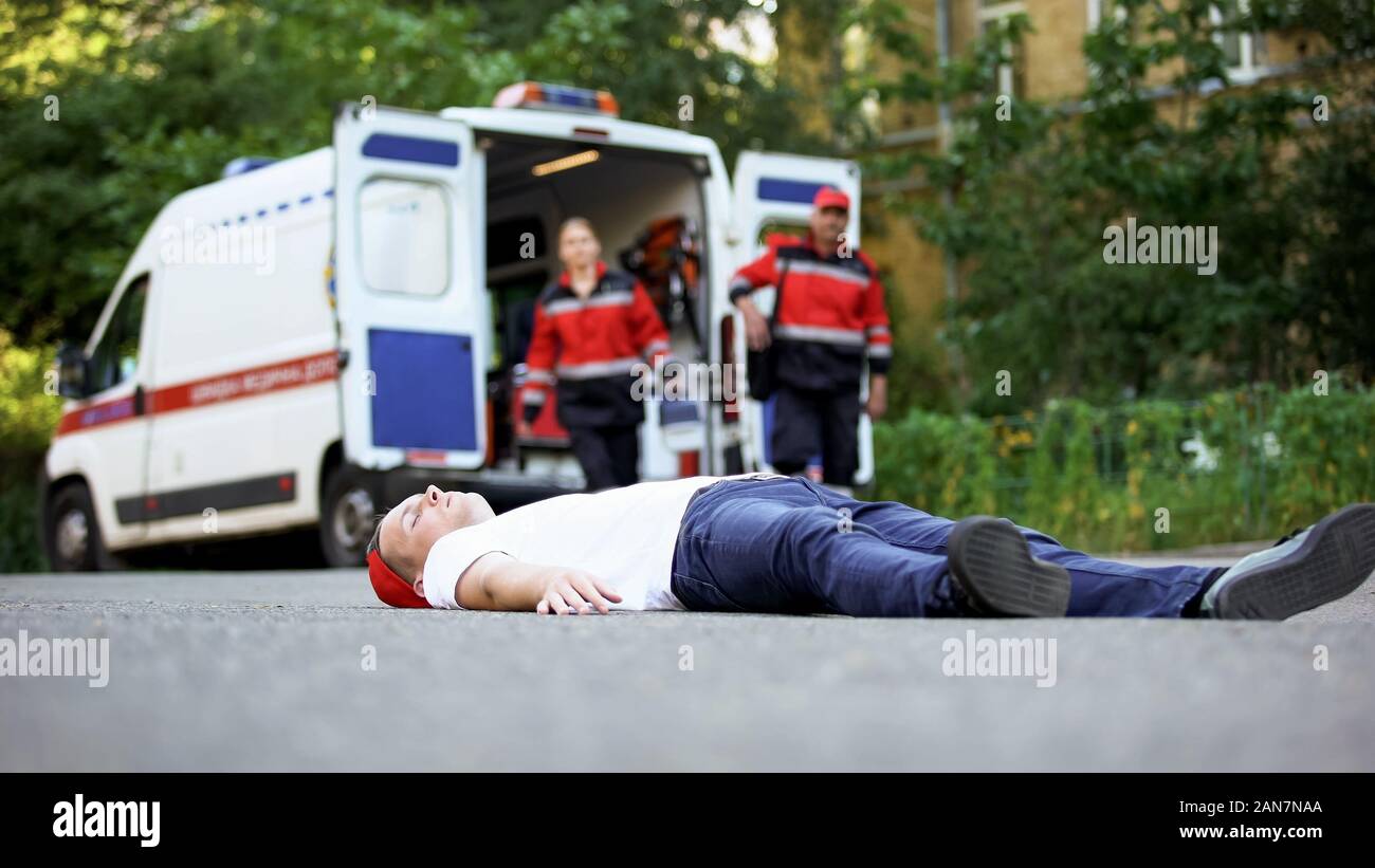 Inconscio uomo disteso sulla strada, paramedici in esecuzione per la vittima di un incidente di automobile Foto Stock