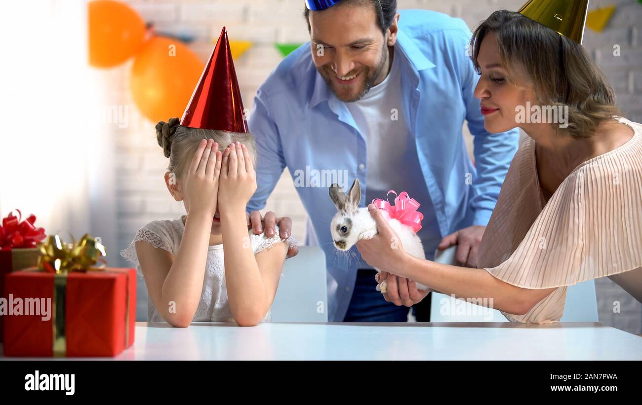 I genitori presentando simpatico coniglietto per la figlia, ragazza con gli occhi chiusi, b-giorni di festa Foto Stock