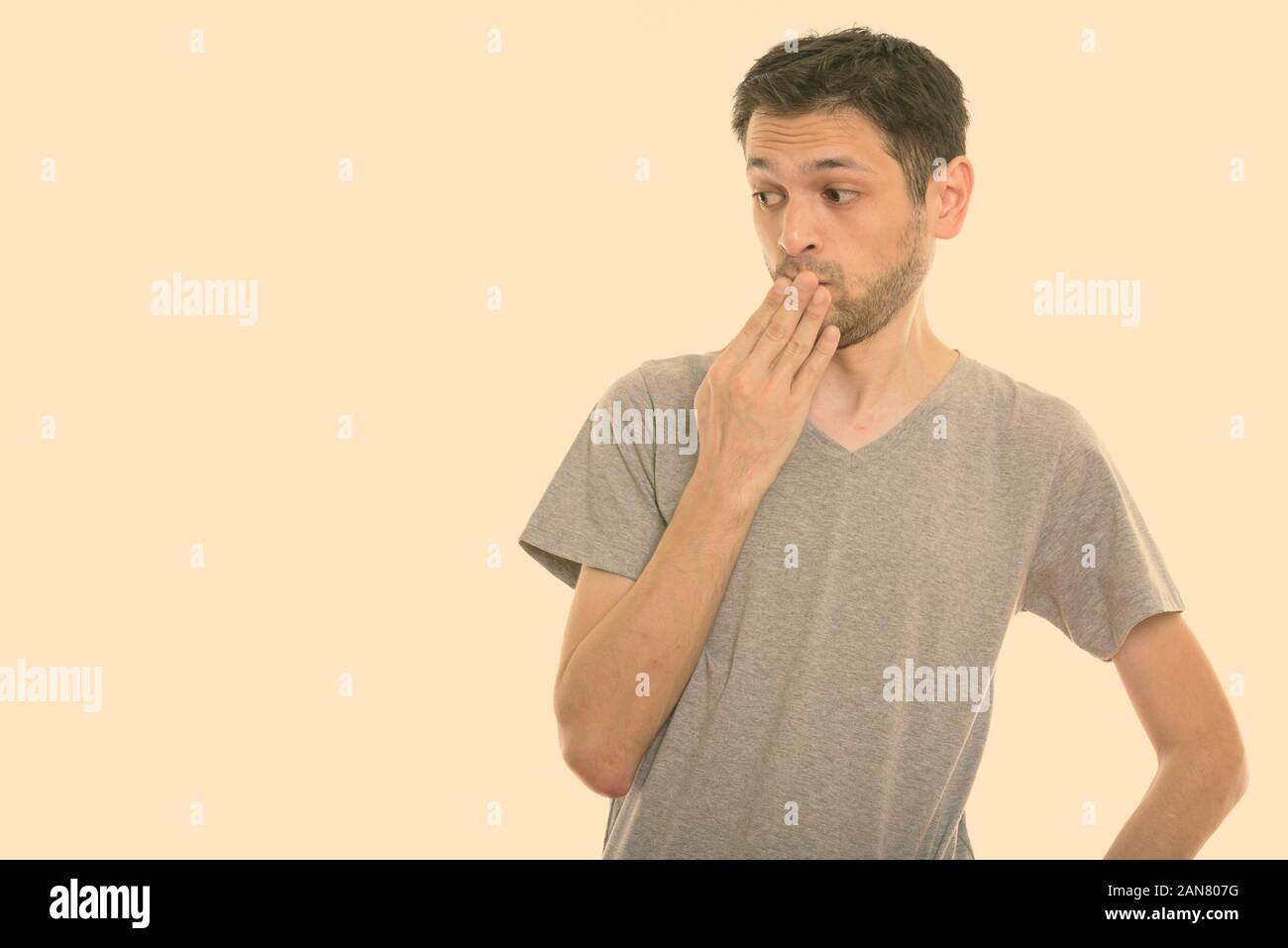 Studio shot di scioccato giovane uomo pensare mentre guardando verso il basso e la bocca di copertura Foto Stock