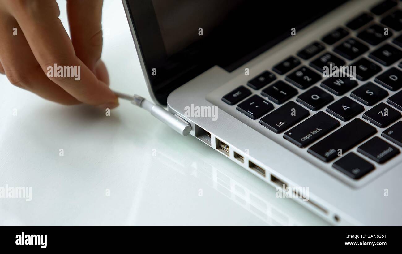 Mano collegando l'adattatore di alimentazione nel computer portatile, ogni giorno la tecnologia del computer per uso personale Foto Stock