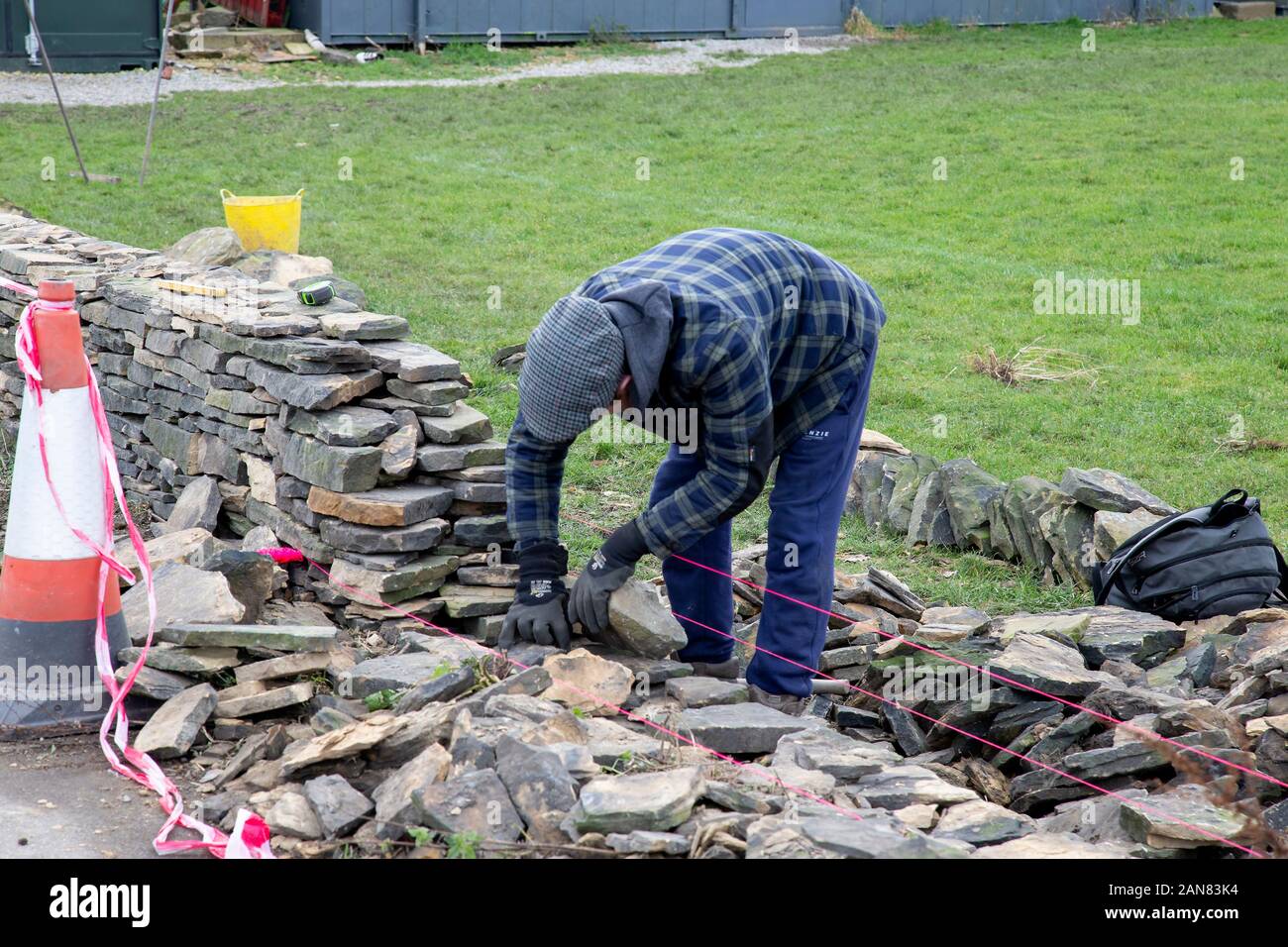 Un secco muro di pietra artigiano di ripristinare una parete diroccata alla sua gloria precedente sul confine di un campo sportivo nel West Yorkshire, Inghilterra, Regno Unito Foto Stock