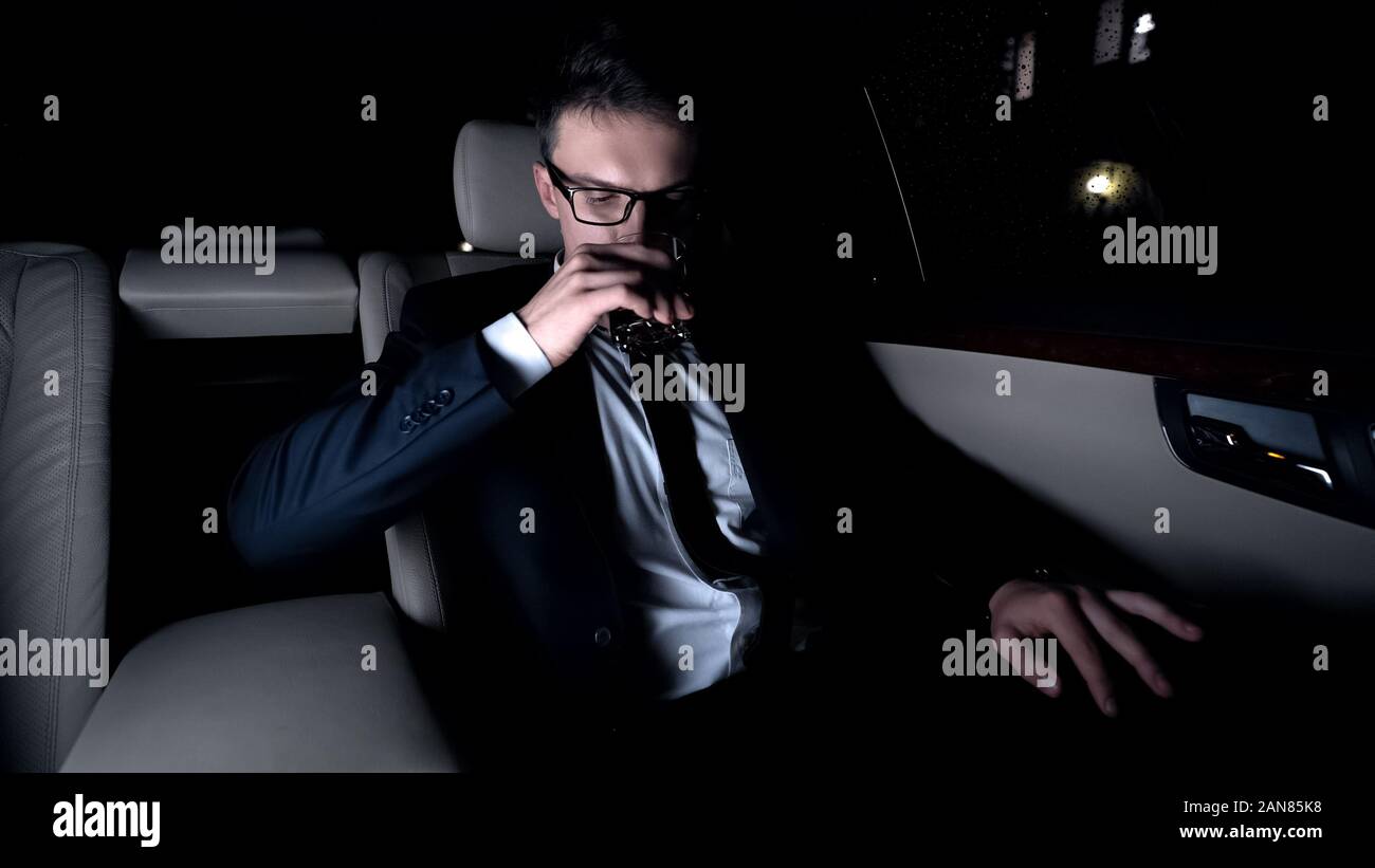 Executive bevanda potabile sul sedile posteriore della vettura, via di casa dopo un duro giorno occupato Foto Stock