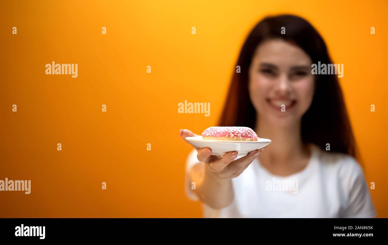 Felice ragazza che mostra una deliziosa ciambella alla telecamera, addolciti snack, rischio di obesità Foto Stock