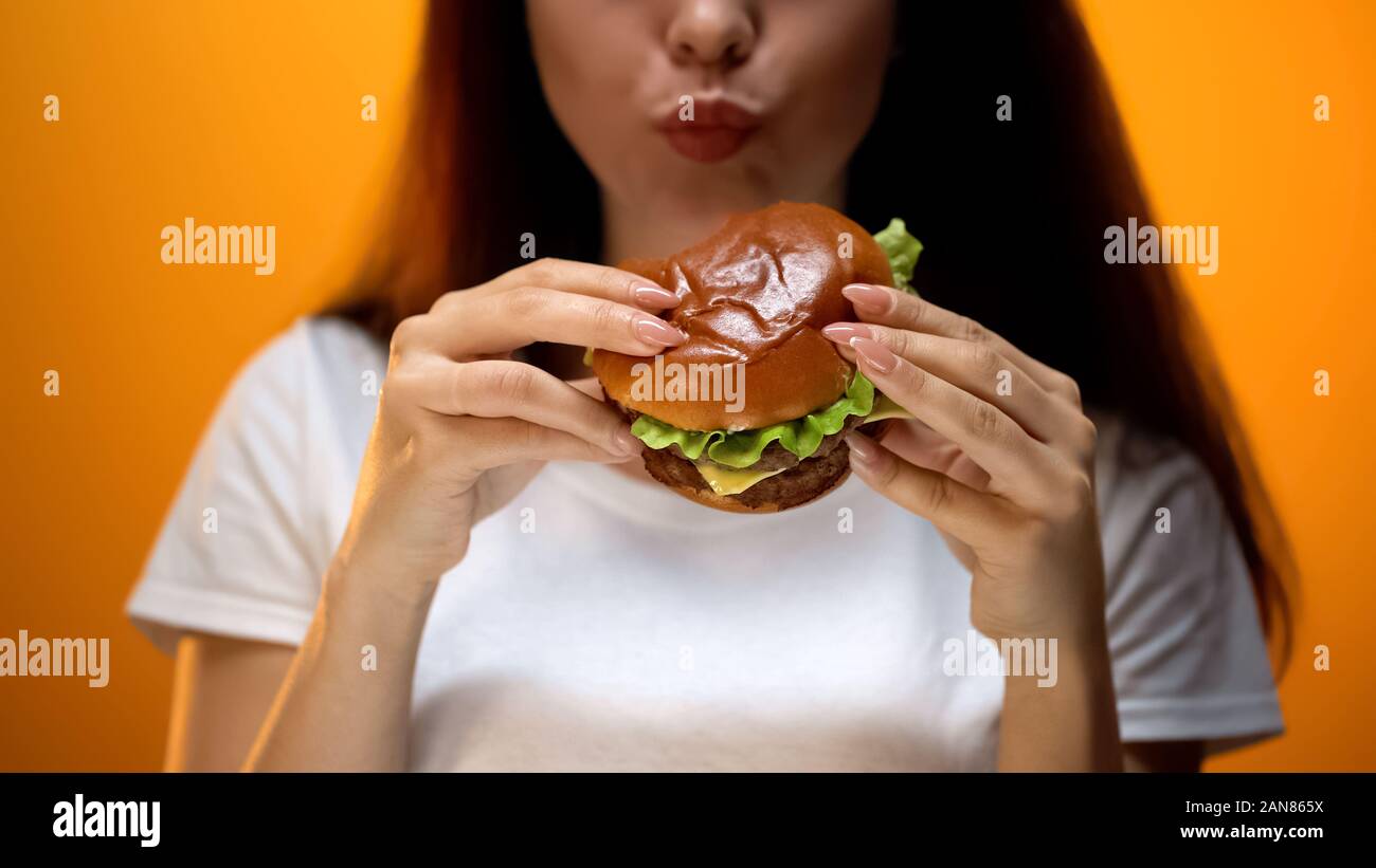 Signora masticare hamburger, ad alto contenuto calorico della nutrizione, rischio di gastrite, problema Foto Stock