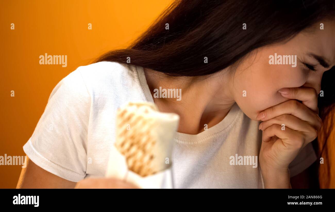 Ragazza sensazione di malessere, tenendo il sandwich, infezioni in cucina di strada e avvelenamento Foto Stock