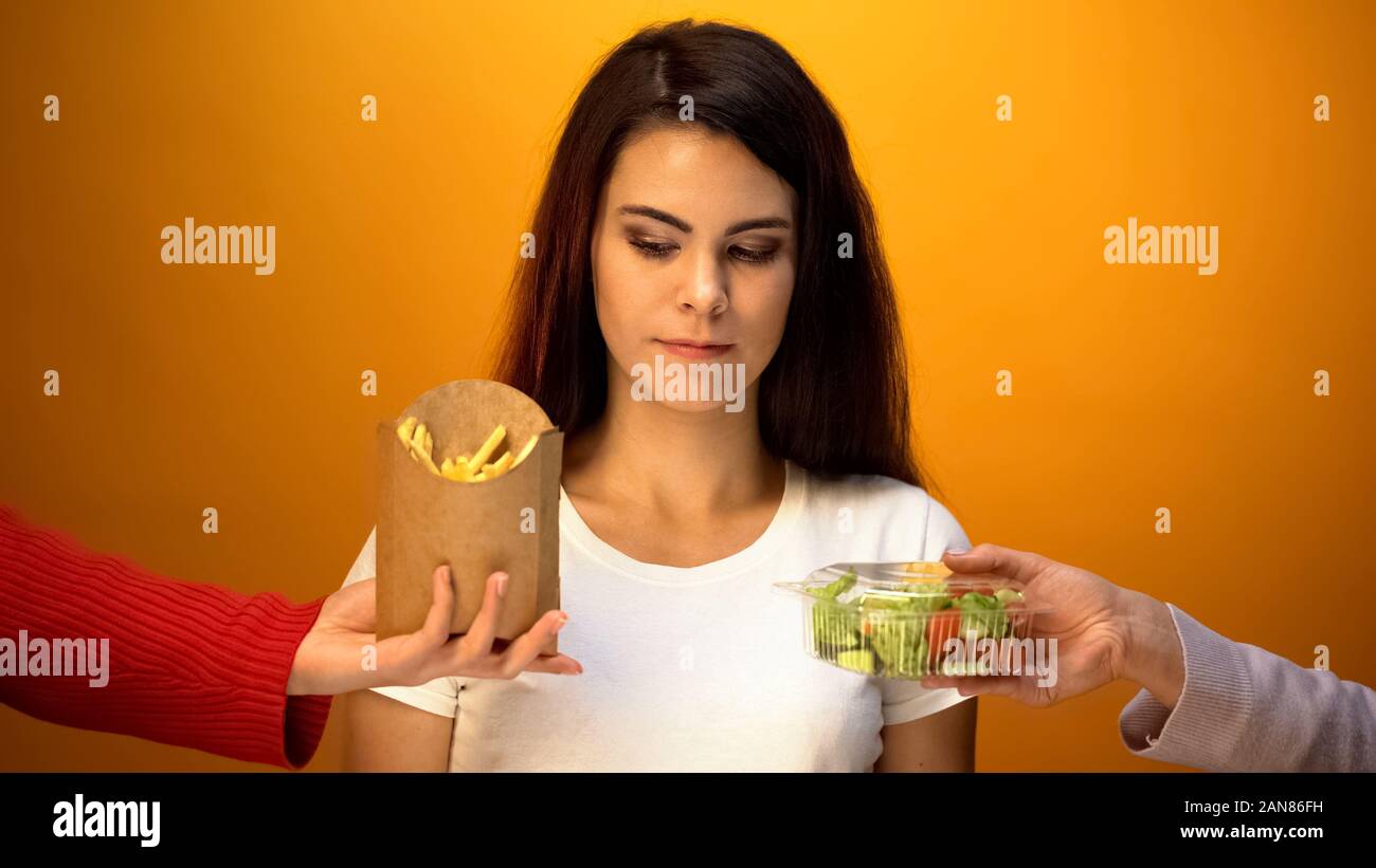 Giovane donna scegliendo tra insalata fresca e patatine fritte, esitano a decidere Foto Stock