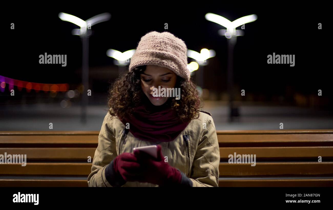 Biracial ragazza seduta all'aperto, guardare immagini divertenti e sinceramente sorridente Foto Stock