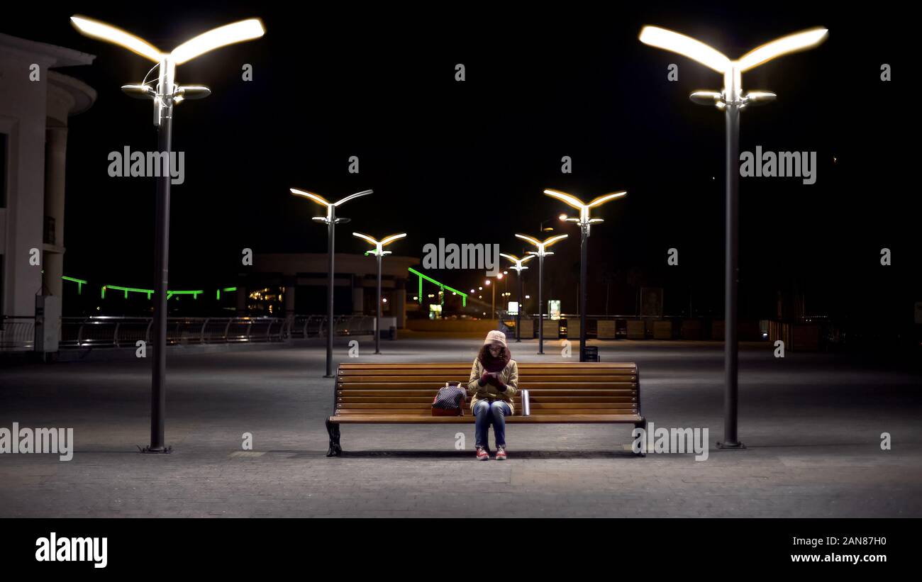Signora congelato in attesa per l'ultimo autobus a vuoto la stazione di notte, controllo calendario Foto Stock