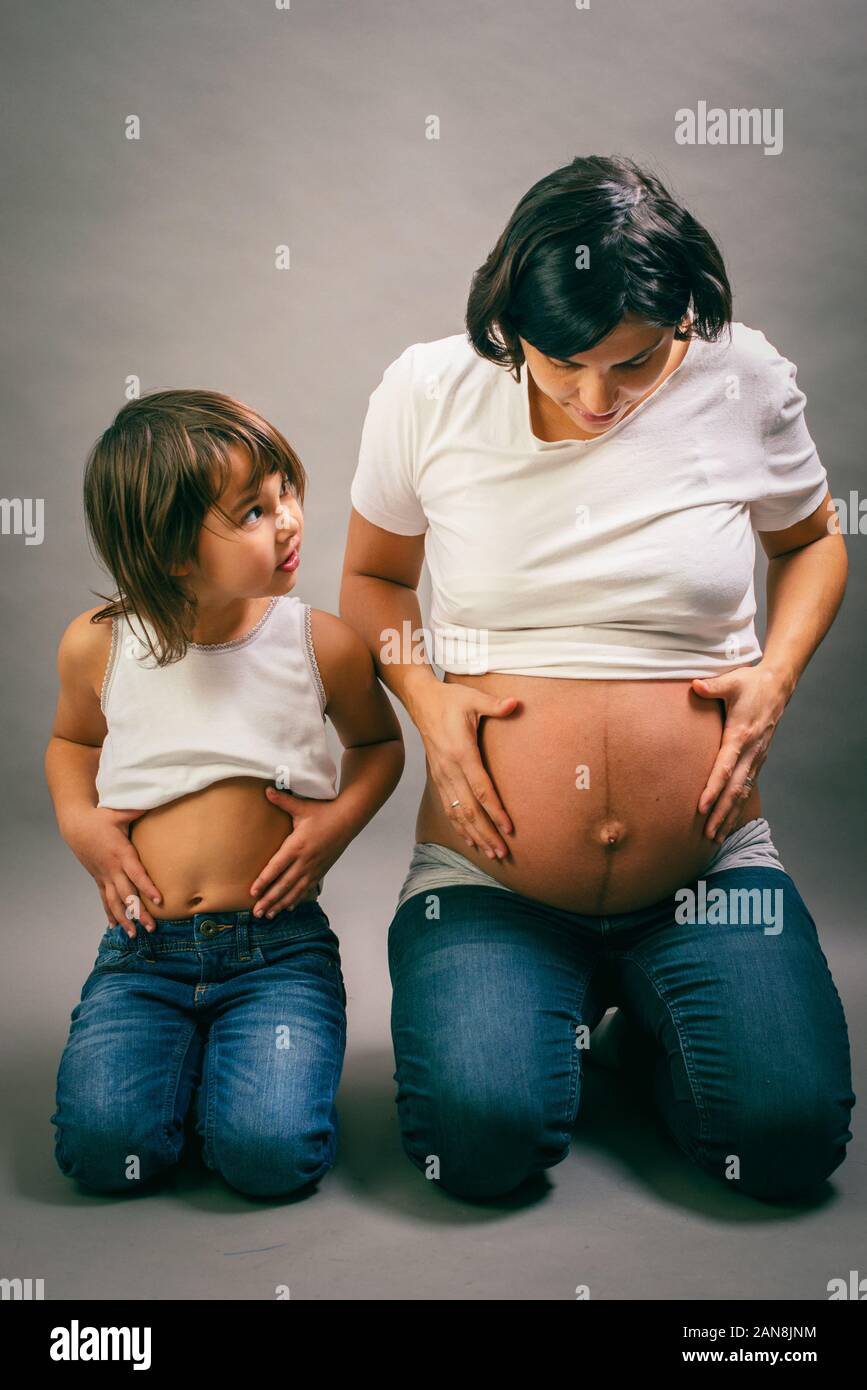 Gravidanza madre e figlia di ridere quando si confrontano le loro pance su sfondo grigio Foto Stock