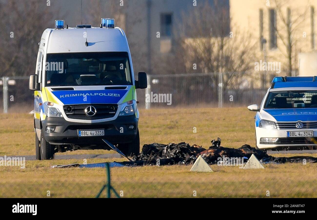 Strausberg, Germania. 16 gennaio, 2020. Tra due veicoli della polizia i resti carbonizzati di un piccolo aereo può essere visto sui motivi di Strausberg airfield. Due persone sono morte nel crash di un piccolo aereo all'aeroporto in Strausberg, Brandenburg. Come il dipartimento dei vigili del fuoco ha inoltre annunciato il giovedì, non altre persone sono state ferite nell'incidente. Perché l'aereo si è schiantato è rimasta poco chiara in prima. Credito: Patrick Pleul/dpa-Zentralbild/ZB/dpa/Alamy Live News Foto Stock