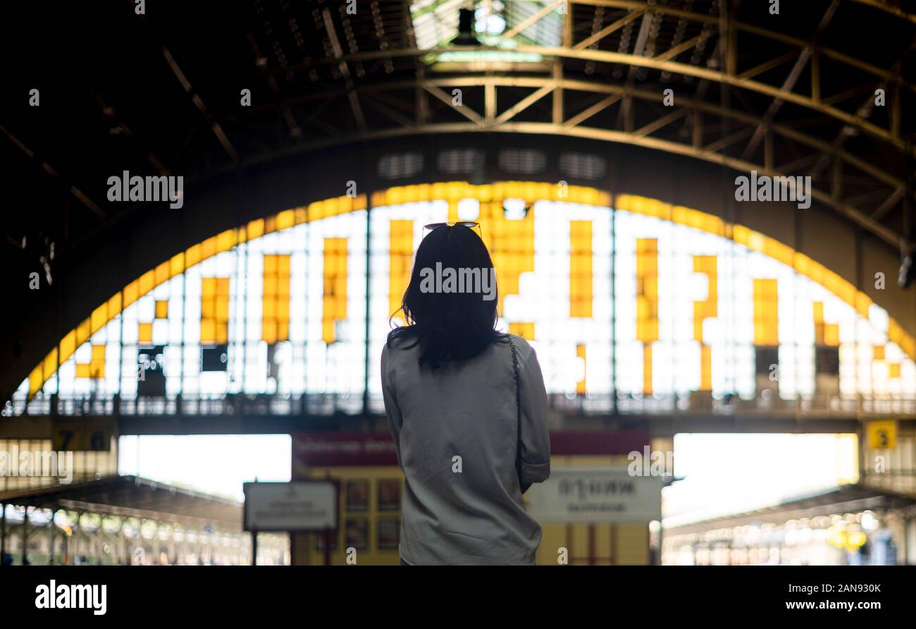Il Nero dei capelli ondulati donna in maglia bianca in piedi nella stazione ferroviaria con tetto a cupola guardando all'uscita. Foto Stock