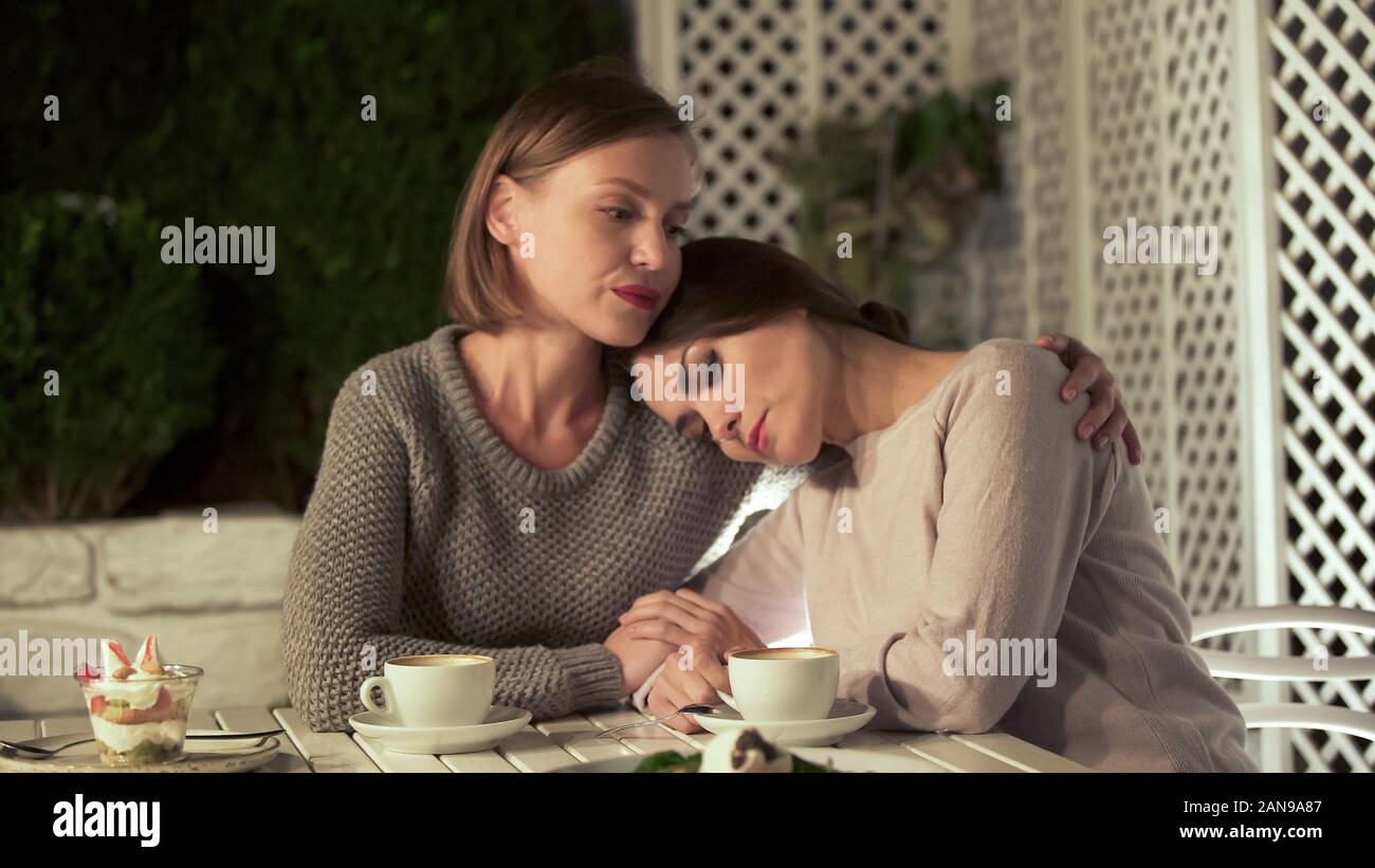 Giovane donna abbracciando triste amico femmina, seduto fuori sulla terrazza, amicizia Foto Stock