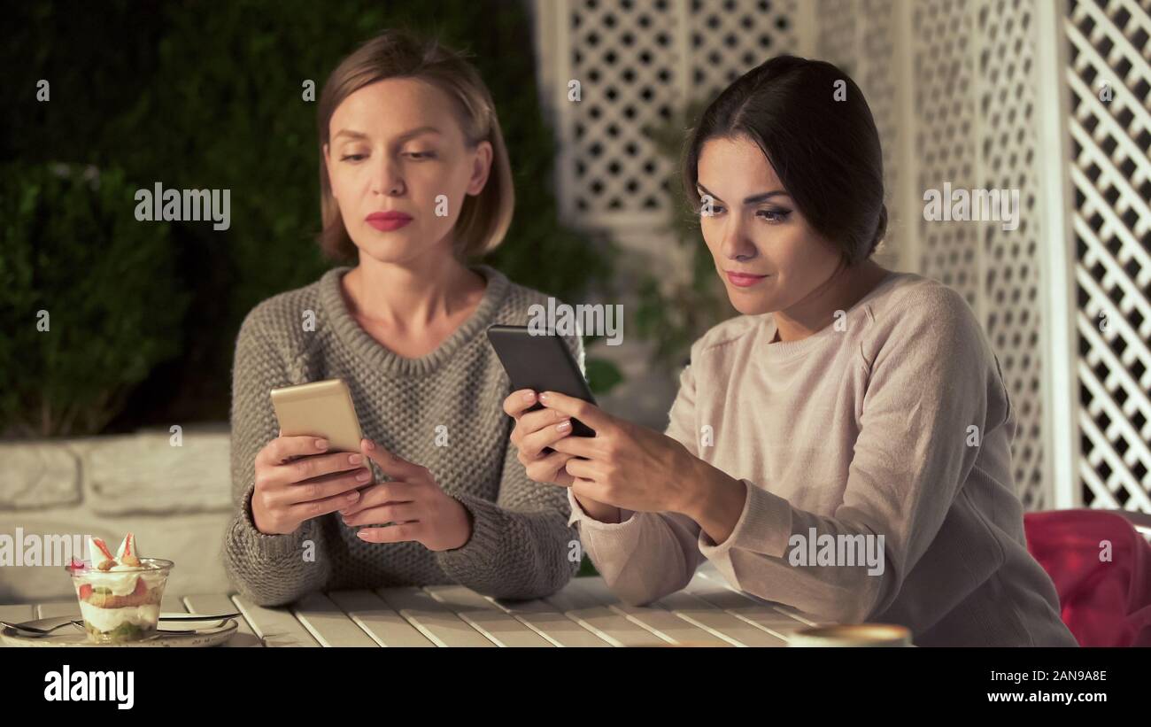 Due signore in chat su telefoni invece live communication, gadget dipendenza Foto Stock