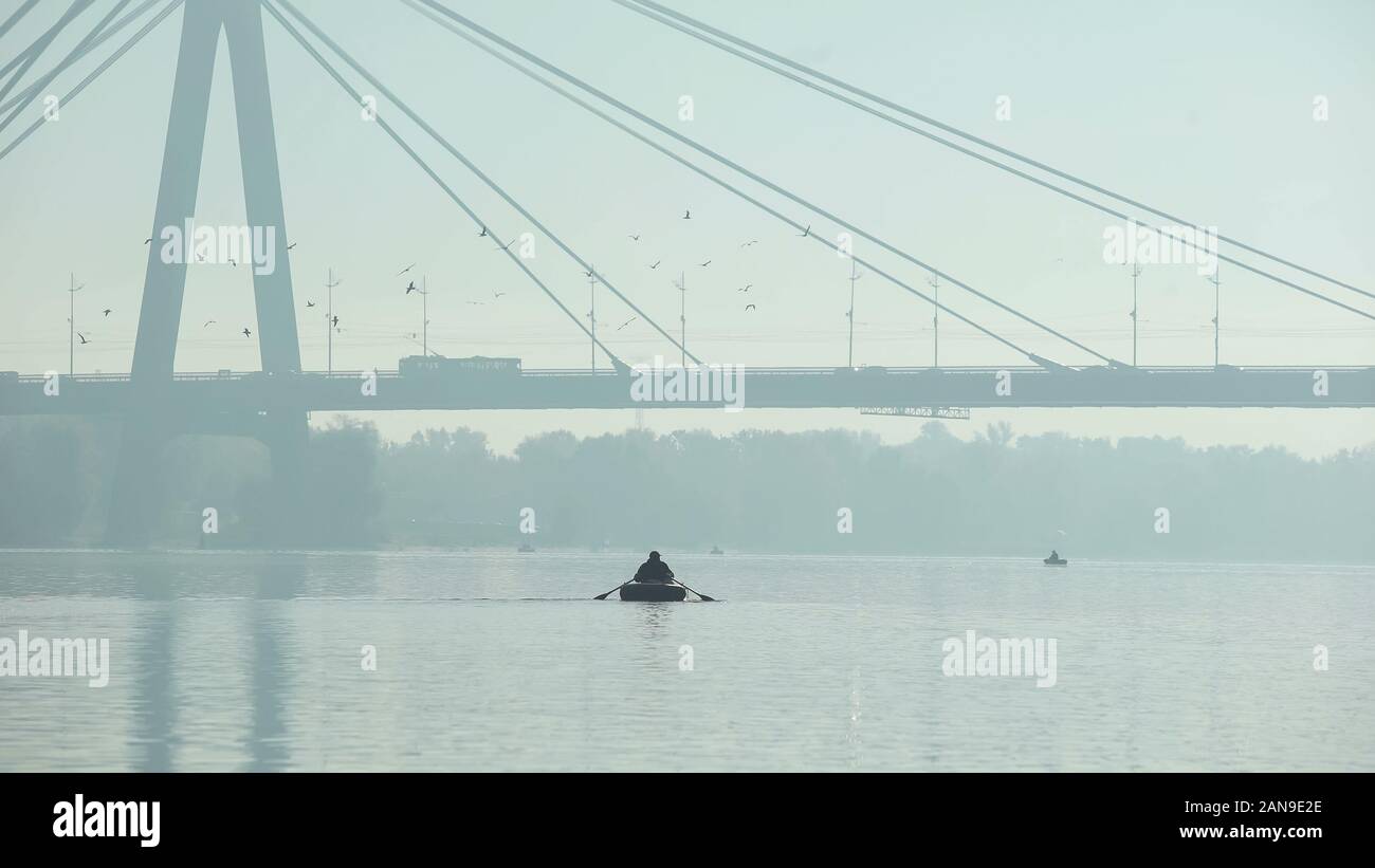 Fisherman vela sotto il grande ponte sul gommone misty meteo, grande città Foto Stock