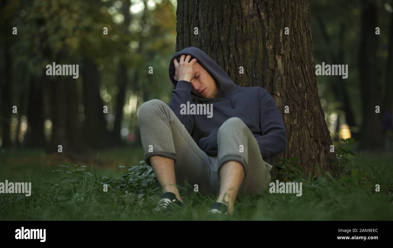 Uomo malsano sbornia nel parco, seduto sotto agli alberi dopo buona parte, malattia Foto Stock