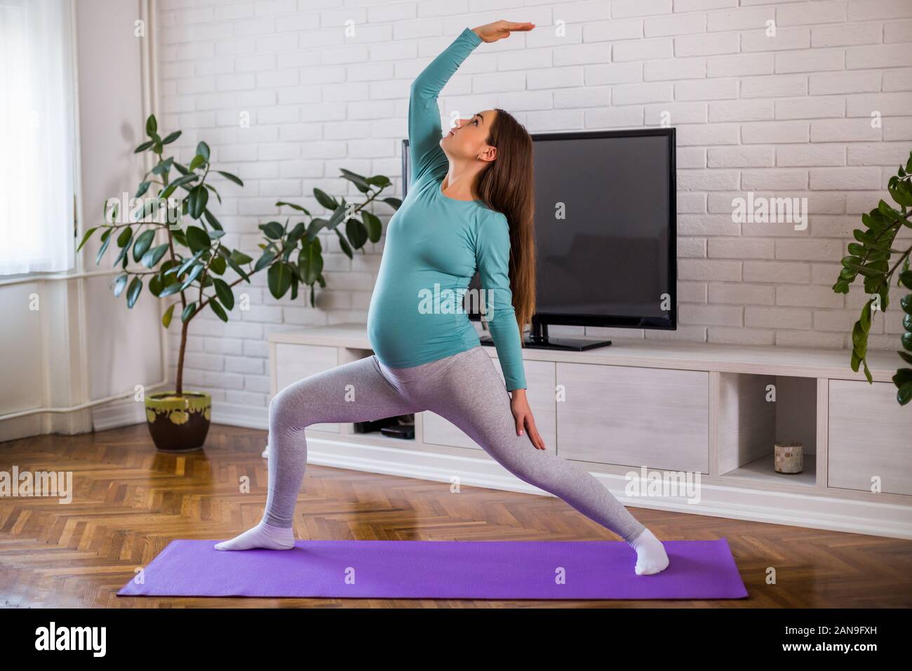 Bella donna incinta gode di esercizio di yoga a casa sua.Virabhadrasana/Warrior pongono Foto Stock