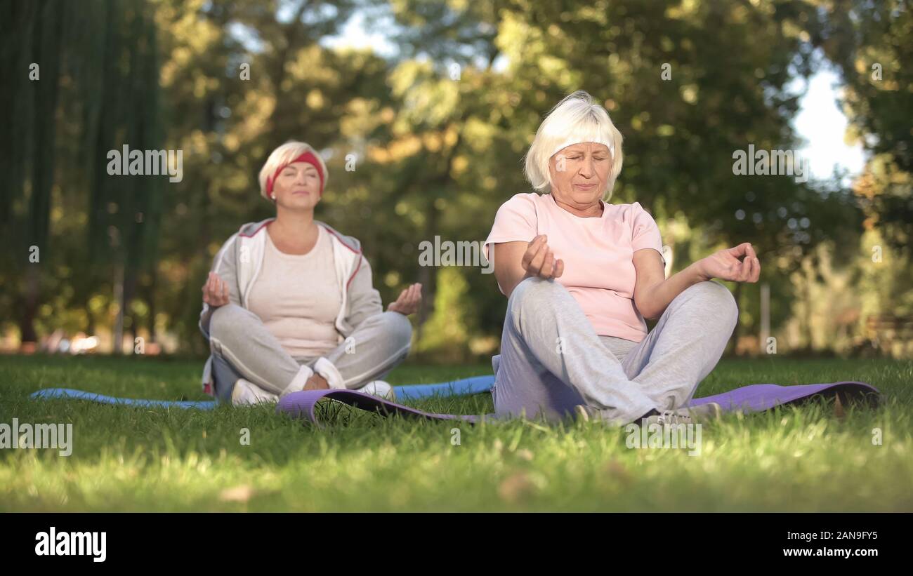 Donne anziane seduti nella posizione del loto e meditando facendo yoga nel parco, energia Foto Stock