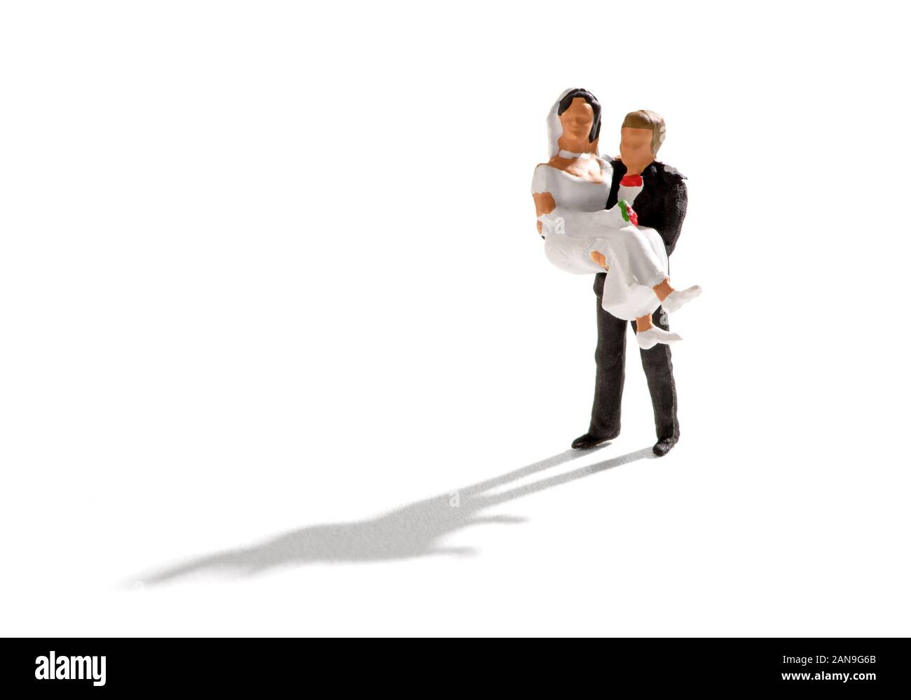 Appena sposati in scena con una scopa tenendo la sua sposa nelle sue mani. Piccolo popolo miniatura isolato su sfondo bianco con lunga ombra Foto Stock