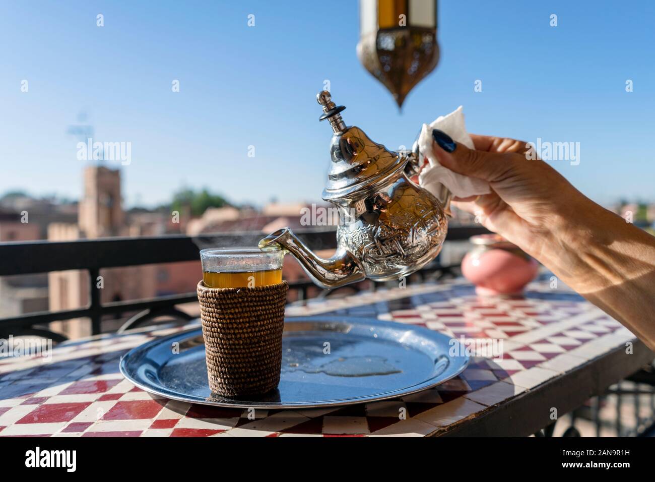 Versando tè marocchino da argento bollitore per il vetro sul tetto di Marrakech, Marocco Foto Stock