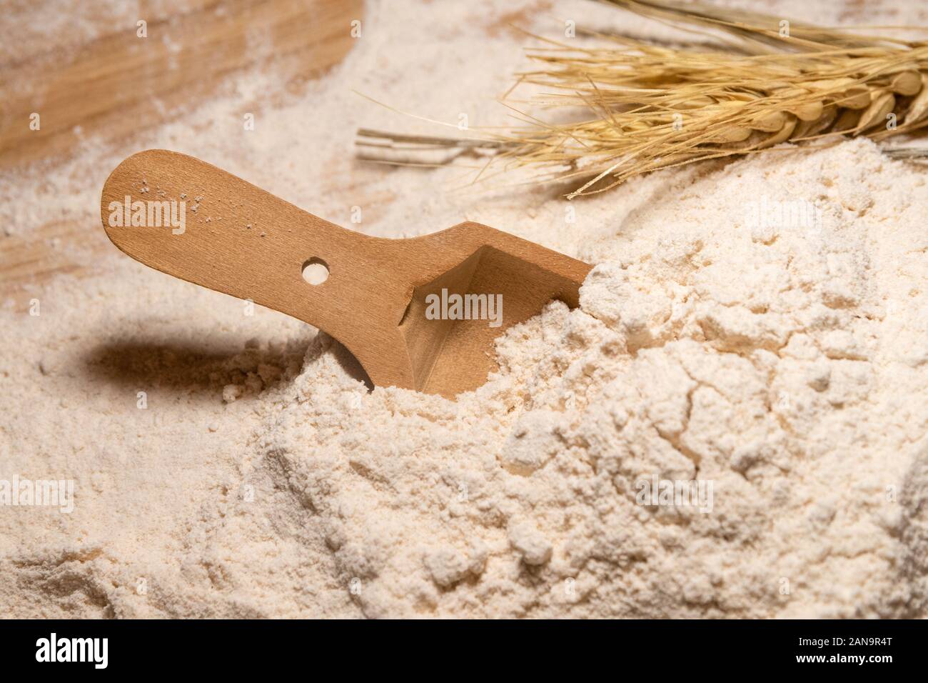 Un cucchiaio di legno in appoggio in una pila di tutta la farina di grano tenero. Foto Stock